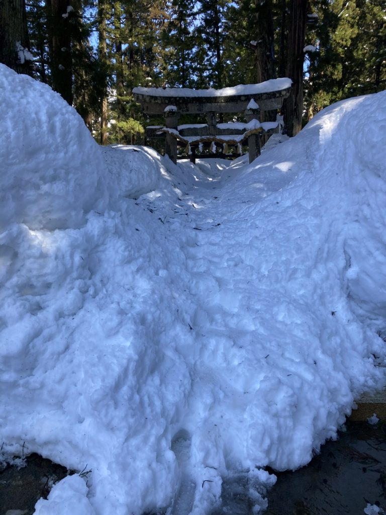 Deep snow near the base of Mt. Hakkai (Hakkaisan 八海山) in Minamiuonuma, Niigata, Japan. The traditional torii gate is buried in snow. Makeshift stairs have been carved in the snow to approach the torii gate.